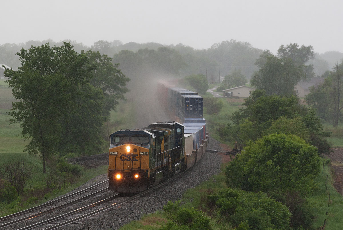 CSXT 7781
In a heavy rain, CSXT 7781 heads east under the bridge at N 350 W nearing Albion. Area is known as the Blue Grass Cut.  05/31/15
