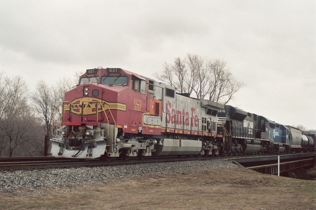 Santa Fe C44-9W #621
Still decked out in original ATSF Warbonnet colors, BNSF C44-9W #621 leads a nearly new NS SD70M-2 #2676 and dead in tow NS (Conrail) GP40-2 #3004 from Jackson over the Kalamazoo River with mixed freight 39J.  The train has just completed making their pickup from Botsford Yard and is now waiting for northbound 36E for Grand Rapids to clear Gibson so the switch can be realigned and they can proceed south.  BNSF power has been fairly common on these trains recently.  39J had 86 cars in this March 31, 2006 photo.  
Keywords: Santa Fe ATSF BNSF Burlington Northern C44-9W Warbonnet 621 SD70M-2 NS Conrail 39J Kalamazoo Botsford