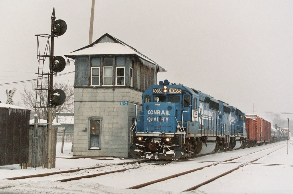 Conrail GP40-2 #3065
NS local job B-1-G shoots past the venerable BO Tower on the Michigan Central mainline at Kalamazoo, MI on January 30, 2007.  This local operates west on Tuesdays and Thursdays to Lawton, Dowagiac, and sometimes as far as Niles. A pair of Conrail painted ITCS equipped GP40-2s are the standard power, often this 3065/3066 set.  They will work Niles today, as evidenced by the Amtrak hopper and boxcars at the headend of the train.  The tankcars are for Welch's in Lawton, and the cars at the tail end go to Dowagiac.  The fresh snow, icicles, and classic mast signal add to this scene.
Keywords: Conrail Quality CR GP40-2 3065 3066 B-1-G B1G BO Tower interlock junction diamond signal mast Kalamazoo